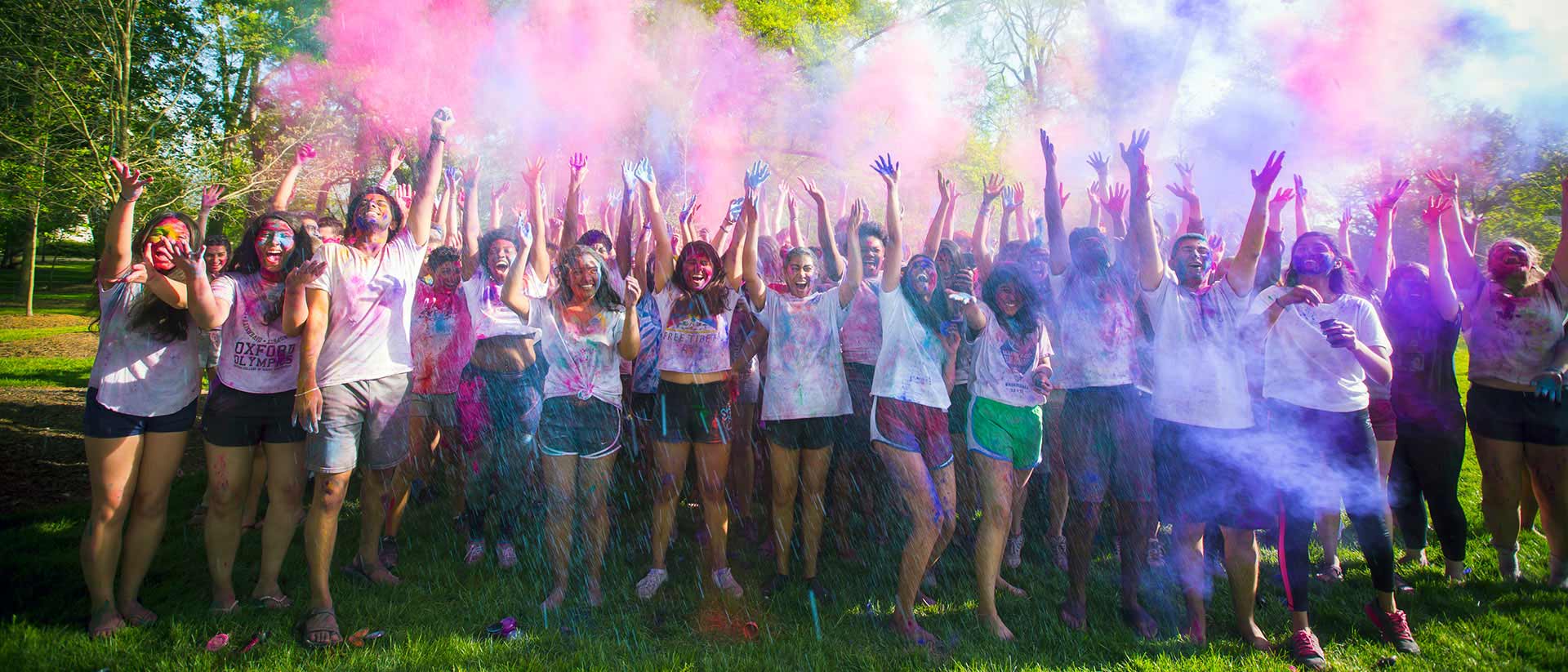 Dozens of students celebrating on campus with colorful smoke or mist.