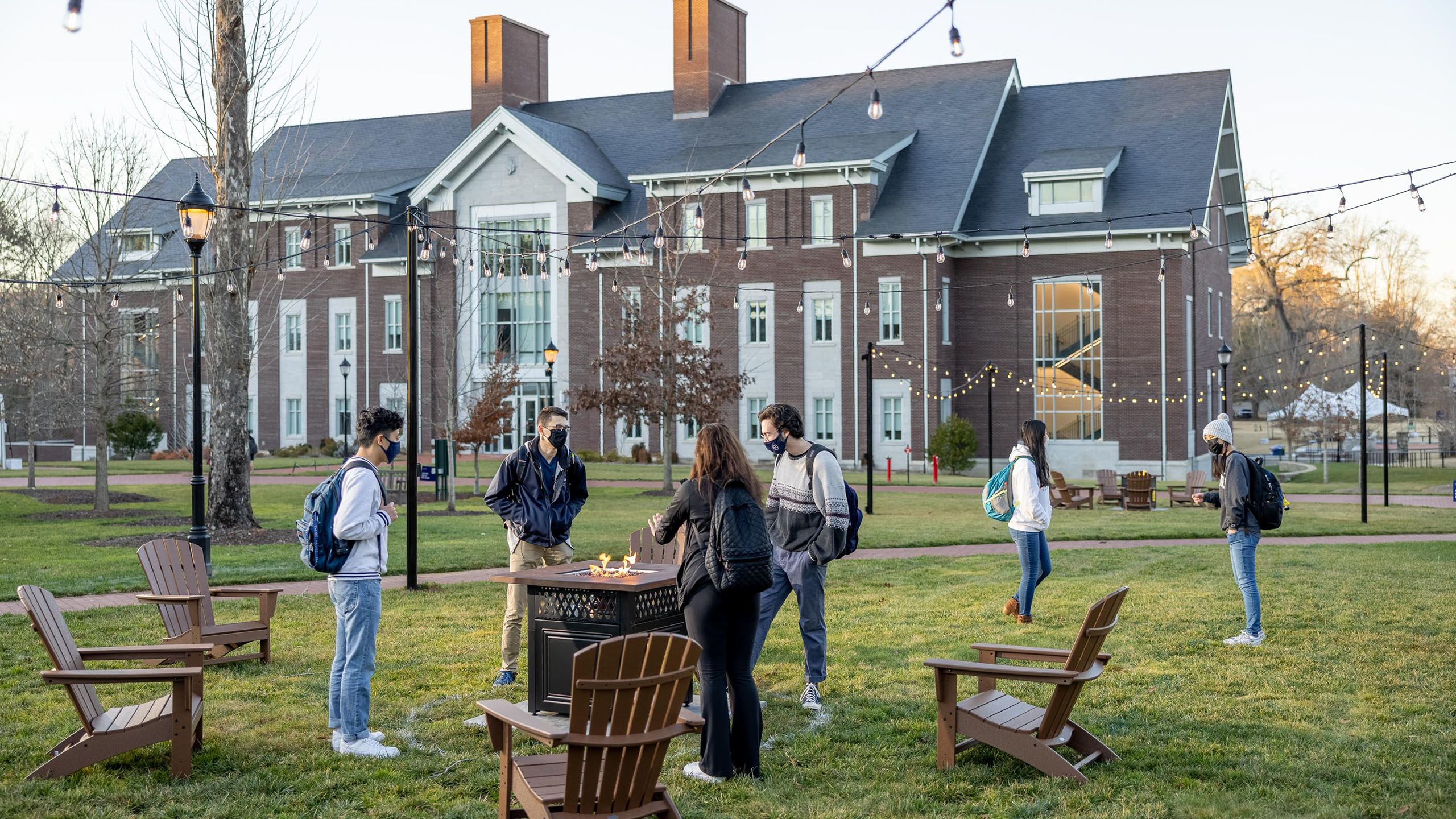 4 students gather around a fire pit near the Oxford Science Building.