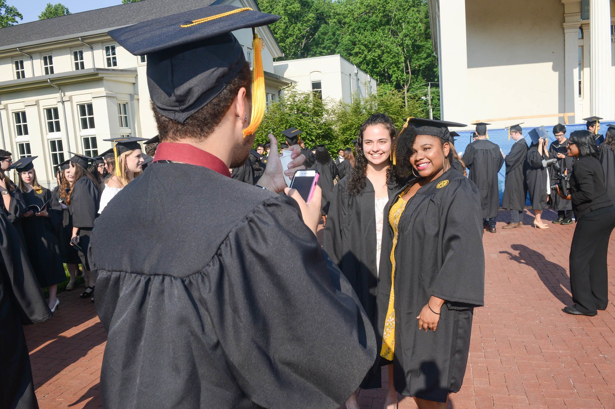 Recent graduates take selfies in front of Phi Gamma Hall.